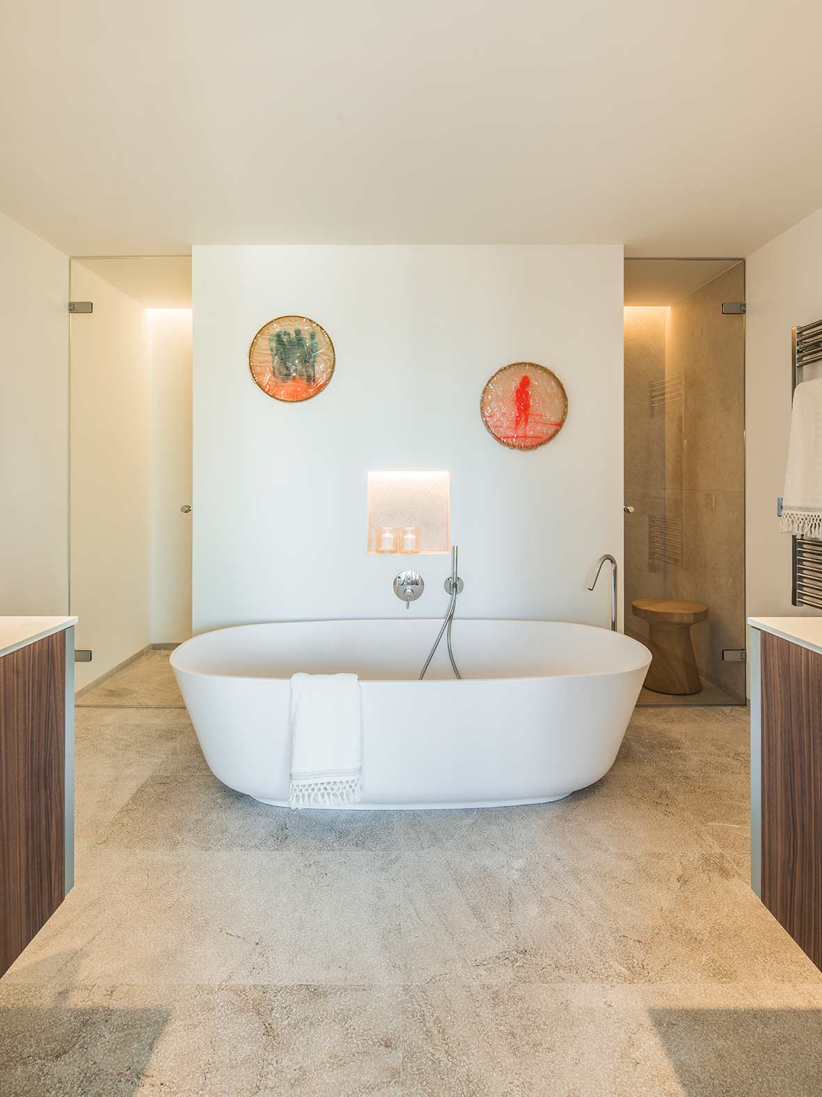 Bad mit weißer freistehender Badewanne vor einer Wand mit beleuchteter Nische und hellem Steinboden