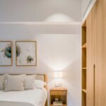 Schlafzimmer mit Bett mit gepolstertem Kopfteil, schwebendem Holznachttisch, abstrakten Bildern und Schrank aus hellem Holz