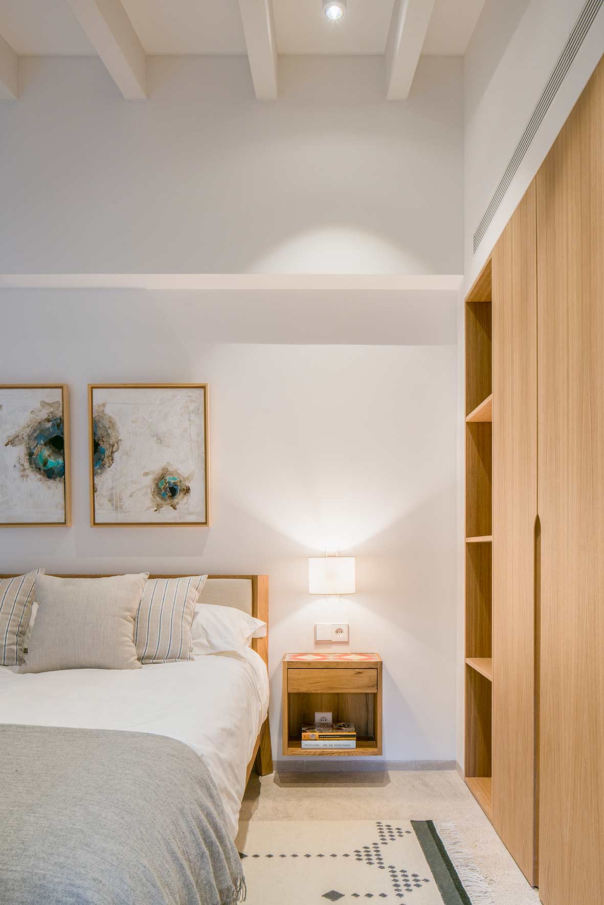 Schlafzimmer mit Bett mit gepolstertem Kopfteil, schwebendem Holznachttisch, abstrakten Bildern und Schrank aus hellem Holz