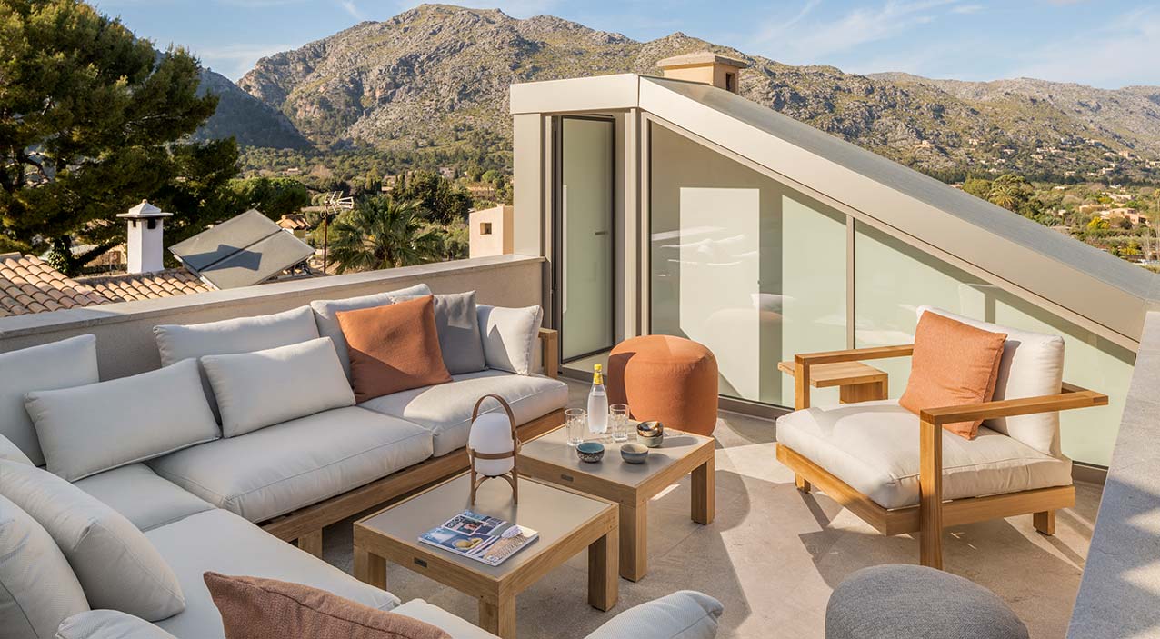 Terraza en la azotea de SJ13 con sofá de exterior, mesas de madera y vistas a la montaña