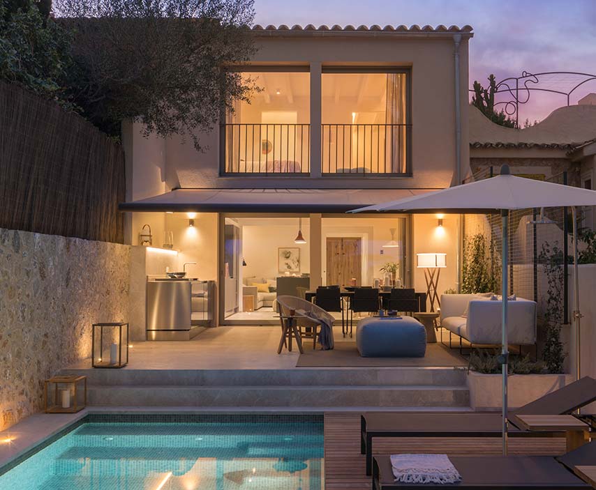 Beleuchtetes Haus in der Abenddämmerung mit gestufter Terrasse, Außenküche aus Stahl und türkisfarbenem Pool