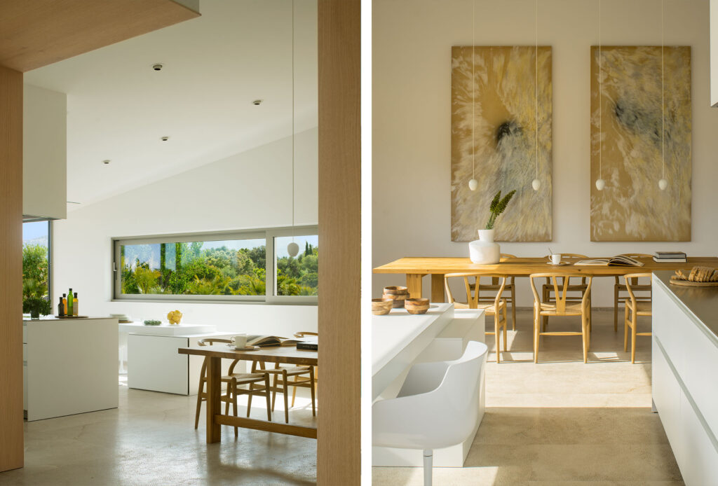 Cocina comedor en díptico, ventana alargada al jardín y mesa de madera bajo dos cuadros dorados