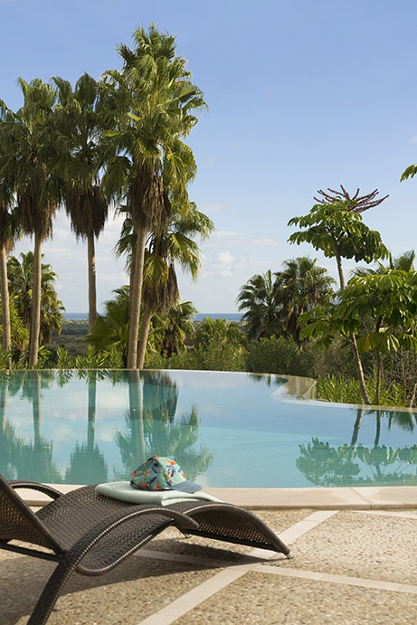 Tumbona de ratán junto a la piscina de borde infinito con palmeras y vistas abiertas al horizonte