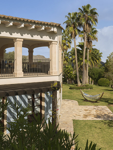 Esquina de la casa con terraza cubierta, pérgola de madera, persianas azules y hamaca sobre el césped