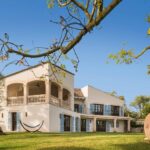 Casa con terraza de arcos y hamaca, con ramas y una gran vasija de barro delante