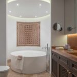 Baño con bañera redonda exenta, mosaico morisco en la pared, suelo de travertino y mueble de madera