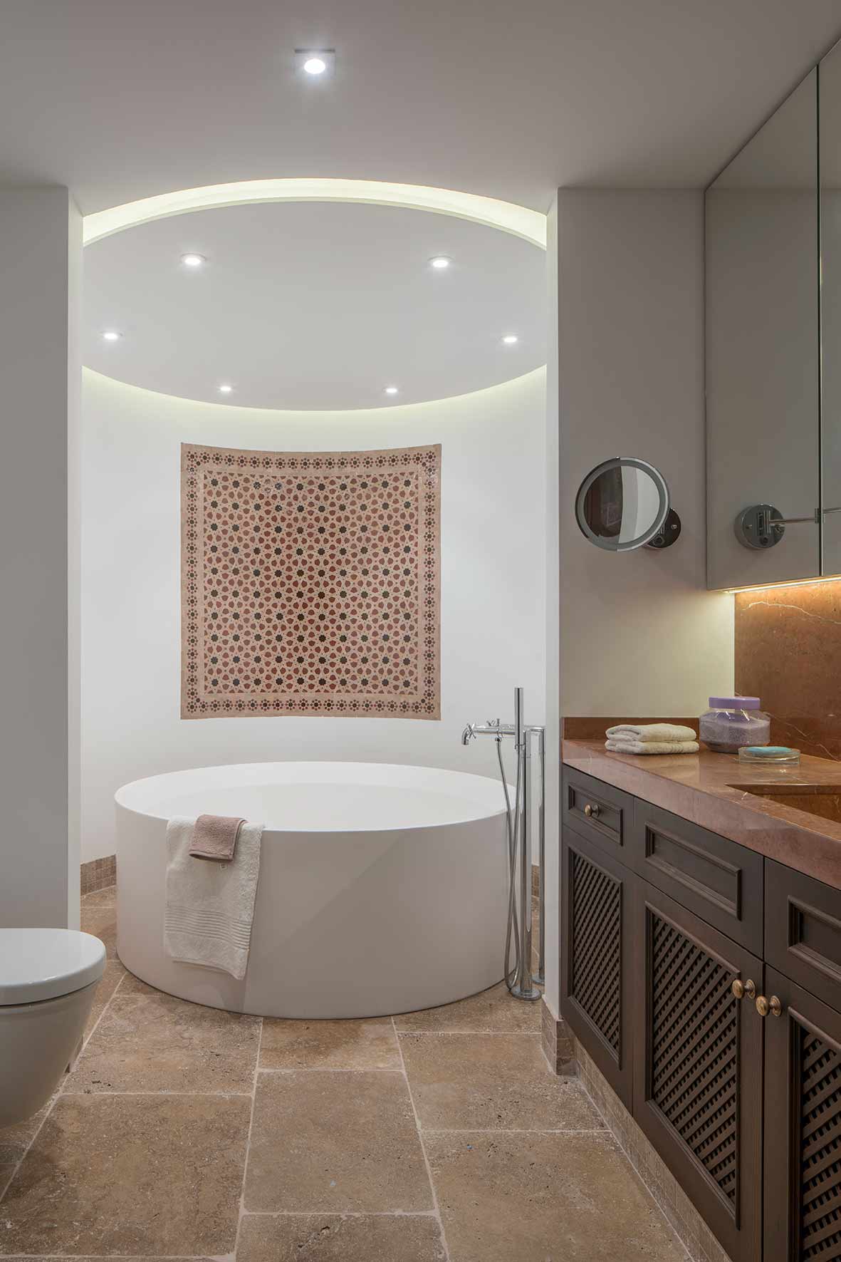 Baño con bañera redonda exenta, mosaico morisco en la pared, suelo de travertino y mueble de madera