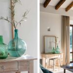 Detalle de garrafones de vidrio verde sobre una consola de madera y rincón del salón con vigas