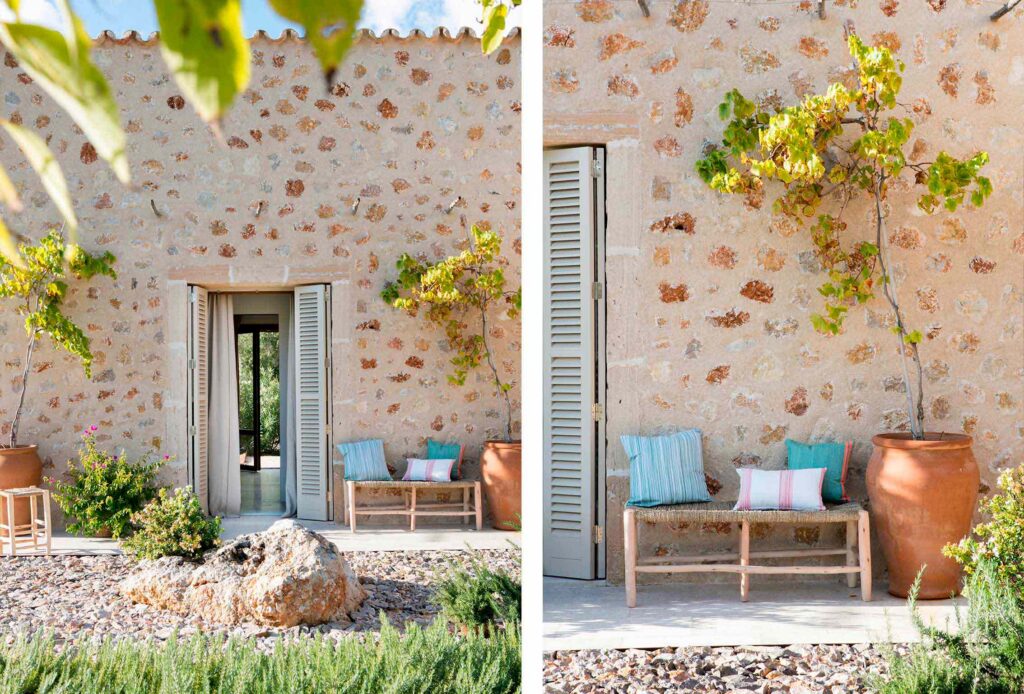 Detalles de la fachada de piedra con contraventanas grises, banco con cojines azules y macetas de barro
