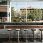 Bar in timber, dark marble and steel with stools in front of the large window at COR Barra i Taula