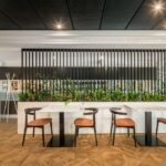 Room with fern planter, black lattice screen, marble tables, chairs with orange seats and parquet