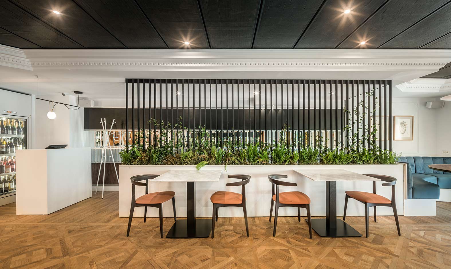 Room with fern planter, black lattice screen, marble tables, chairs with orange seats and parquet