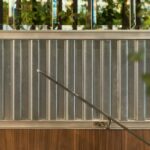 Detail of corrugated metal sheet with bevelled mirrors above, steel handrail and timber panel