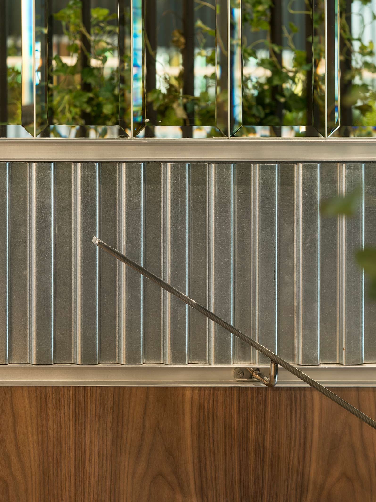 Detail of corrugated metal sheet with bevelled mirrors above, steel handrail and timber panel