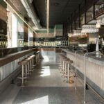 Aisle between two bars with stools, menu boards, green walls and linear ceiling lighting