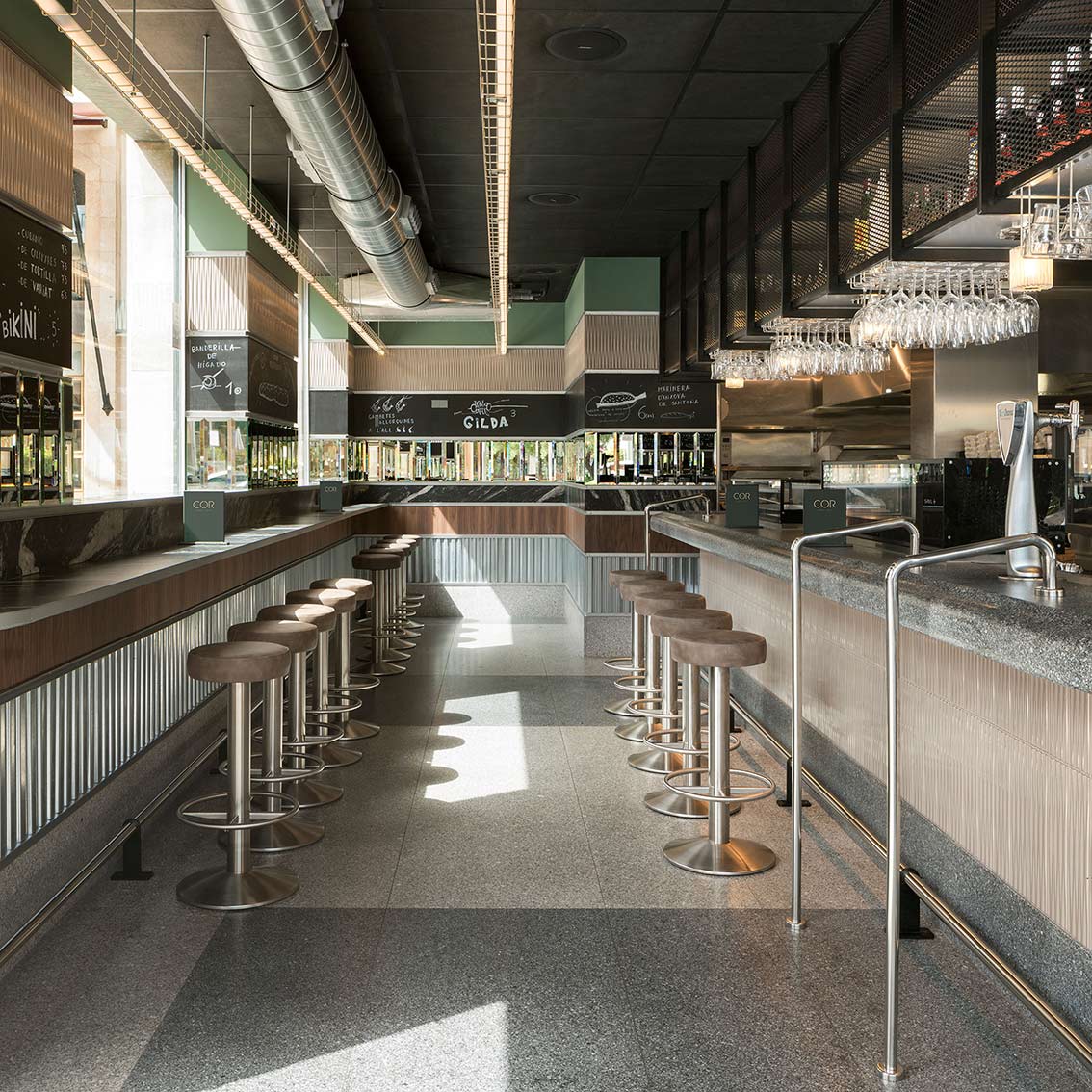 Aisle between two bars with stools, menu boards, green walls and linear ceiling lighting