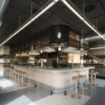Island bar with a hanging black mesh structure, linear ceiling light and stools around it