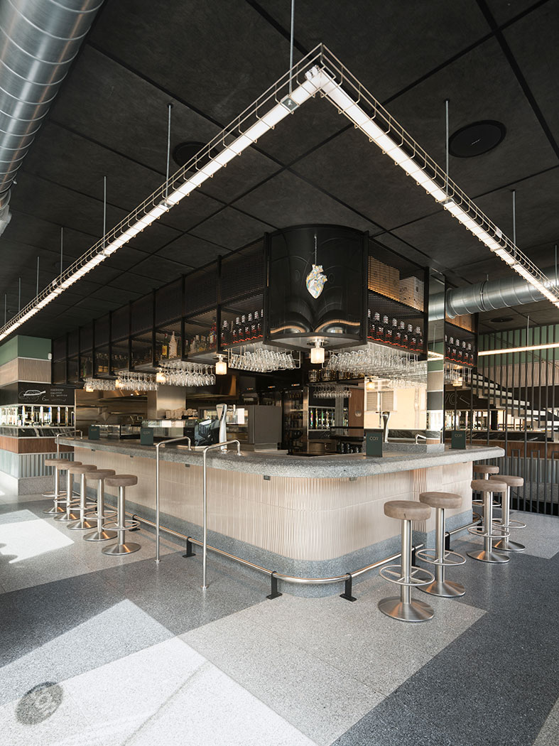 Island bar with a hanging black mesh structure, linear ceiling light and stools around it