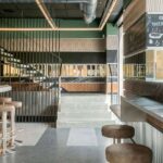 Pale stone steps between a black-barred railing and a bar with stools, beneath a linear light fitting
