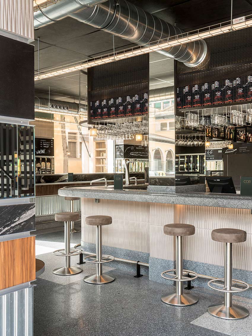 Stone bar with stools, hanging glasses, black mesh shelves and exposed ventilation ducts