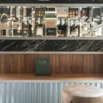 Detail of menu board, bevelled mirrors, black marble and timber over a bar with an upholstered stool