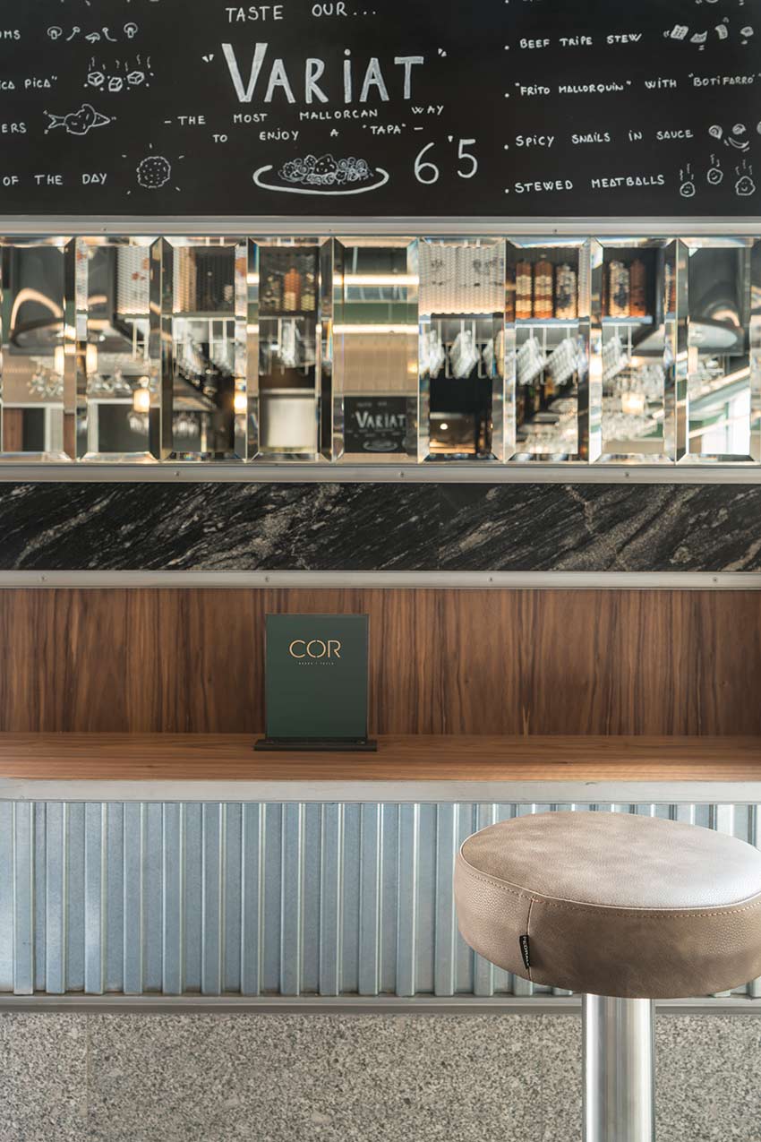 Detail of menu board, bevelled mirrors, black marble and timber over a bar with an upholstered stool