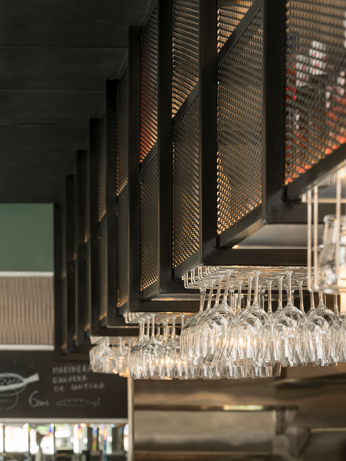 Detail of black metal mesh shelving above the bar with wine glasses hanging