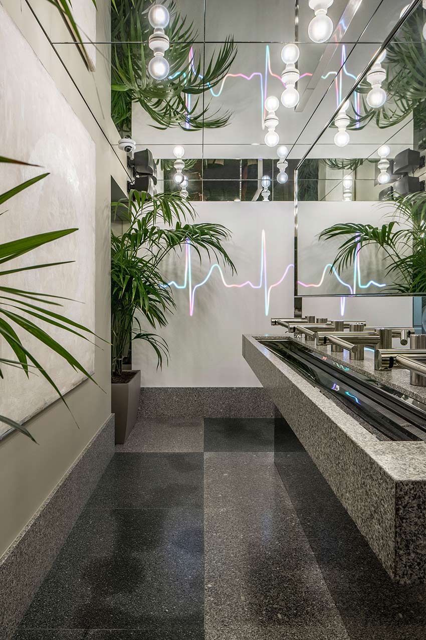 Heartbeat line of light reflected in the washroom mirrors, with palm trees, light bulbs and a stone basin