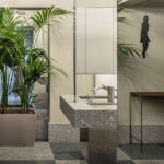 Grainy stone washbasin with mirrored pillar, potted palms and grey chequered floor