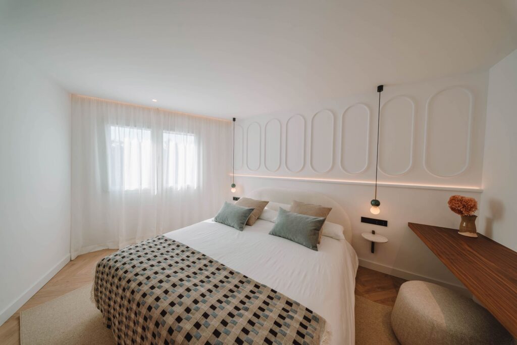 Dormitorio con cabecero de molduras ovaladas, luz indirecta, cortinas de gasa y ropa de cama blanca