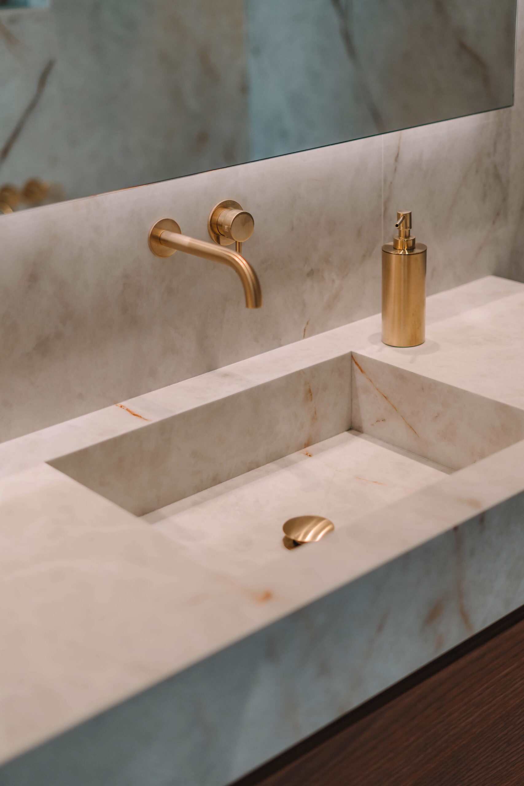 Detalle de baño con lavabo integrado en piedra clara veteada y grifería empotrada dorada