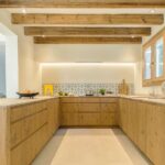 U-förmige Küche mit Holzschränken, heller Arbeitsplatte, sichtbaren Balken und gemustertem Fliesenspiegel