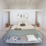 Symmetrisches Schlafzimmer mit Doppelbett, graugrünem Plaid, Bank am Fußende und weißer Balkendecke