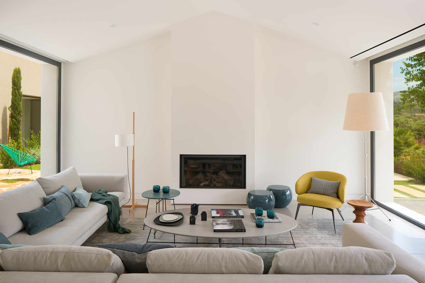 Beiges Sofa und ovaler Couchtisch vor dem Kamin, beidseitig große Fenster zum Garten