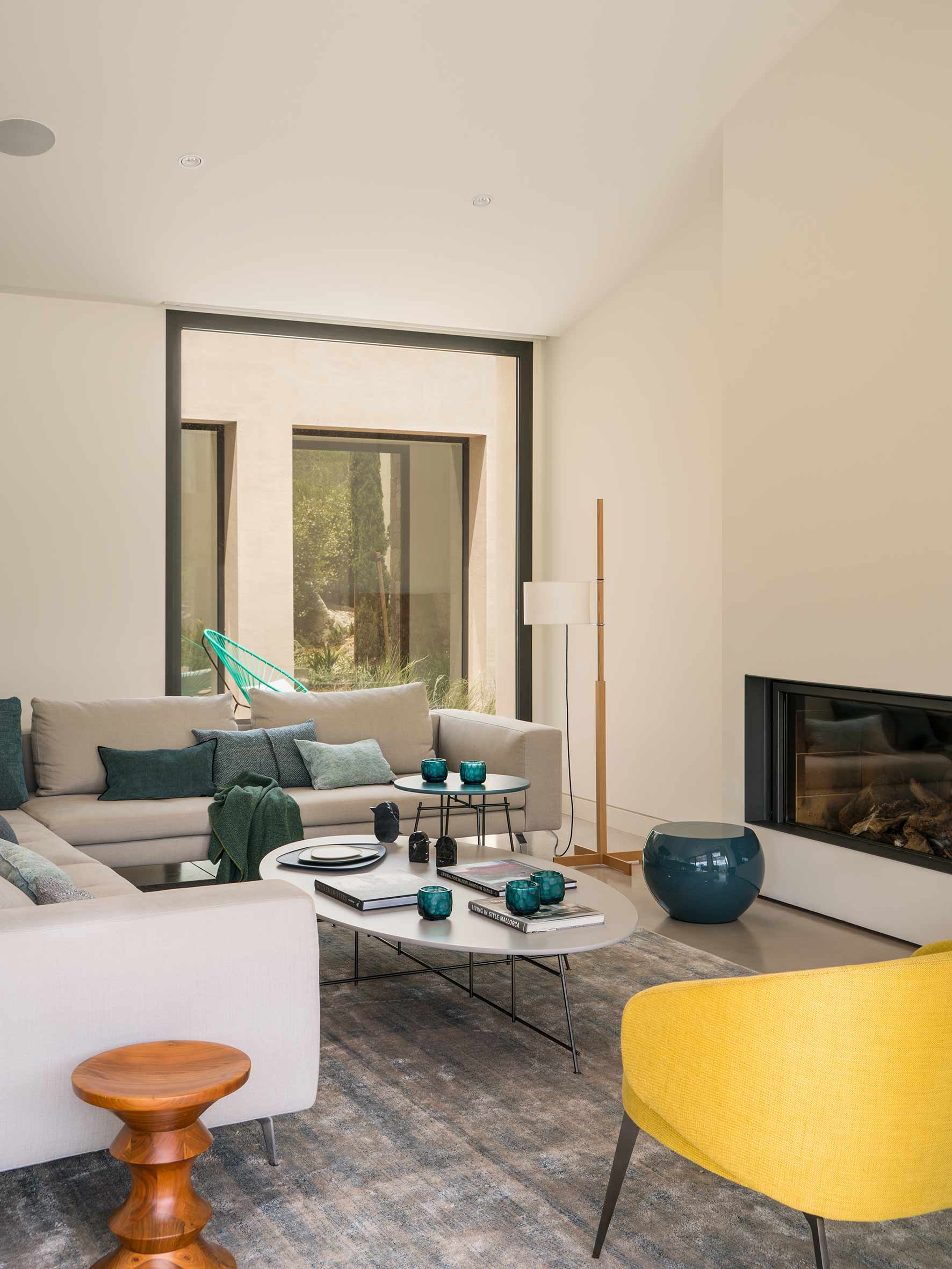 Ecke des Wohnzimmers mit Ecksofa, Holzhocker, gelbem Sessel und begrüntem Innenhof im Hintergrund
