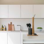 Detail einer weißen Arbeitsplatte mit Holzbrett, Küchenutensilien, Ölflaschen und Schale mit Kräutern