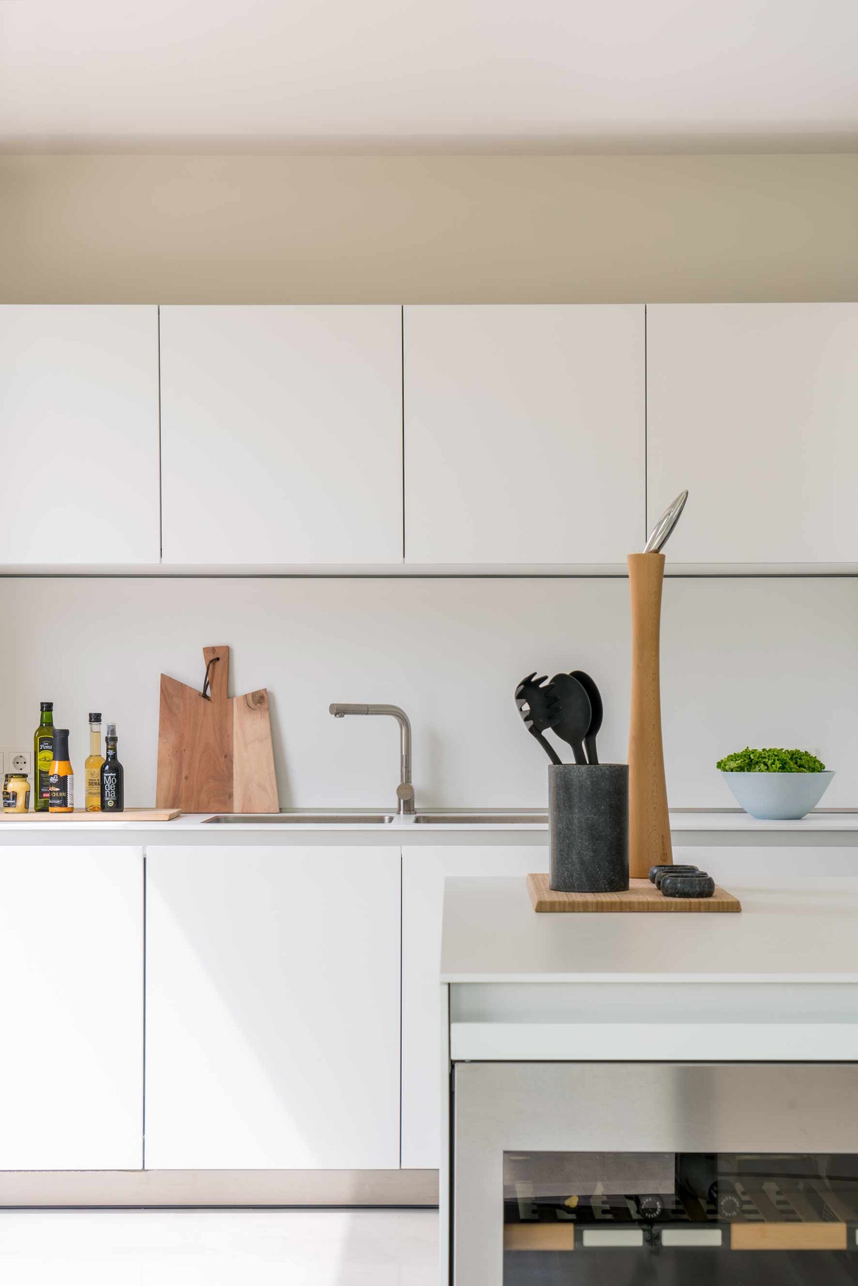 Detail einer weißen Arbeitsplatte mit Holzbrett, Küchenutensilien, Ölflaschen und Schale mit Kräutern