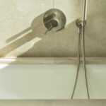Detail der Wandarmatur und Handbrause über der Badewanne, mit heller Steinwand