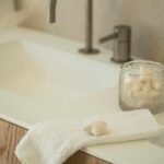 Detail des weißen Waschbeckens mit geschwungenem Wasserhahn, Eichenmöbel, weißem Handtuch und sternförmiger Seife
