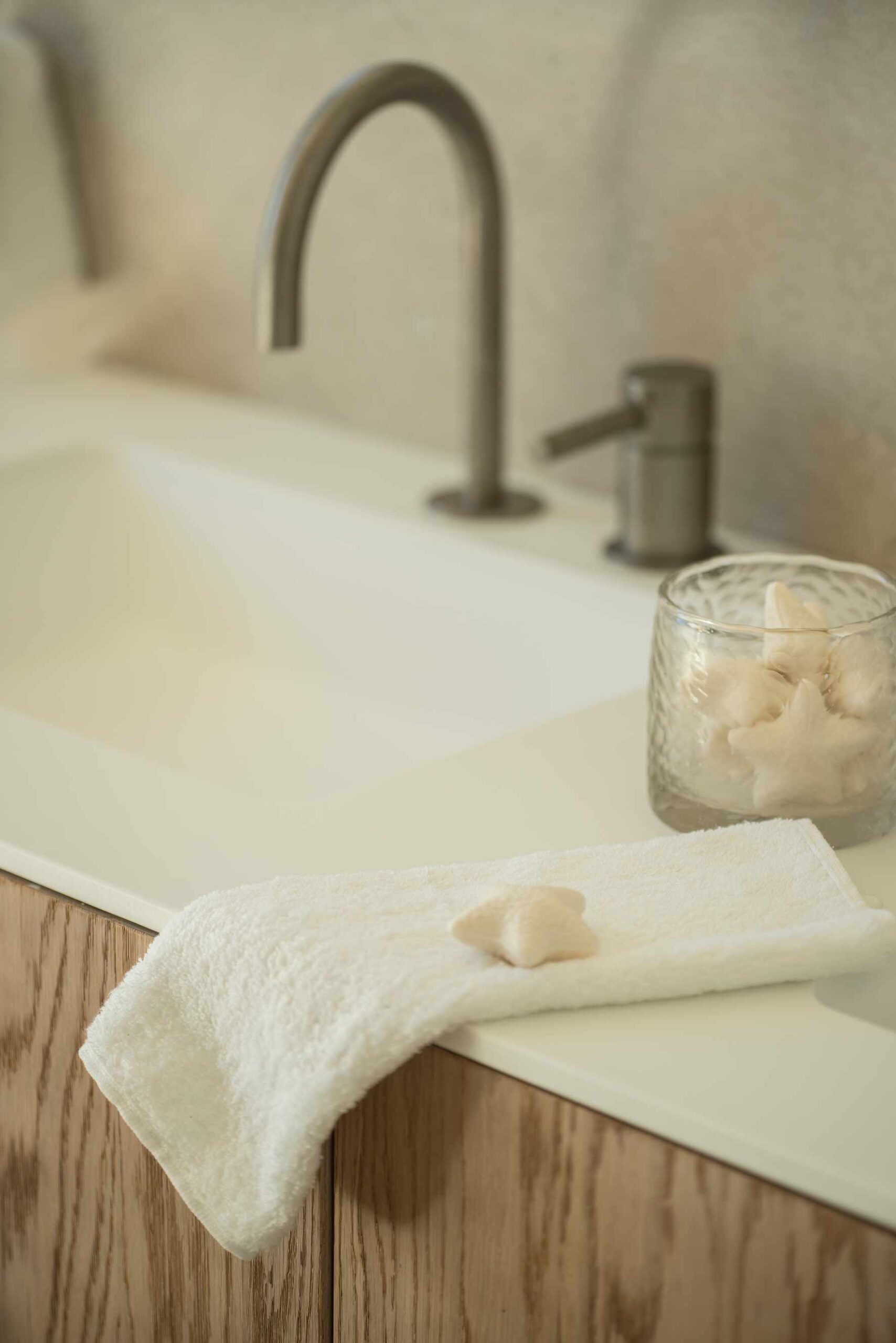 Detail des weißen Waschbeckens mit geschwungenem Wasserhahn, Eichenmöbel, weißem Handtuch und sternförmiger Seife