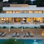 Fachada de Gotmar 142 al anochecer con muro de piedra, piscina y salón acristalado iluminado