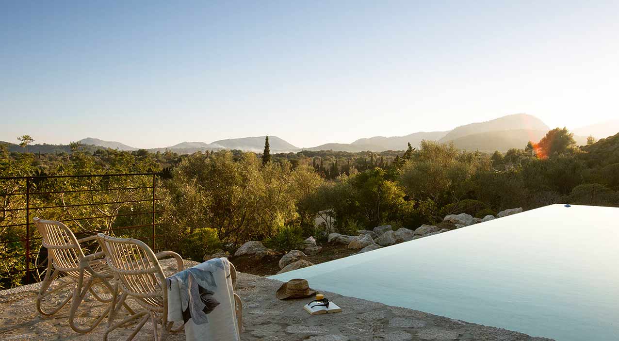 Piscina infinita de Dalt de Can Suau con sillas de ratán y montañas al atardecer