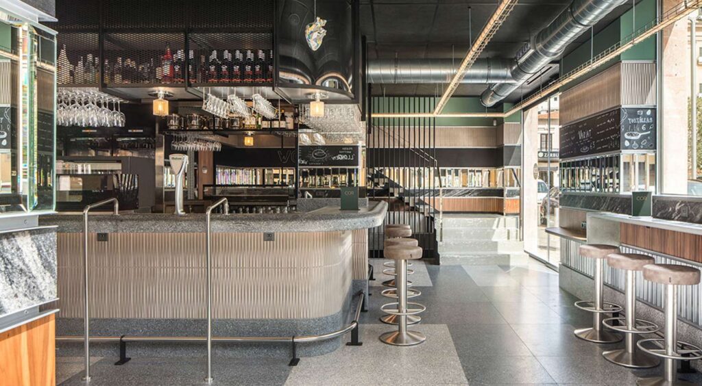 Curved bar with fluted front and stone top, stools, bottles and staircase beyond