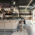 Curved bar with fluted front and stone top, stools, bottles and staircase beyond