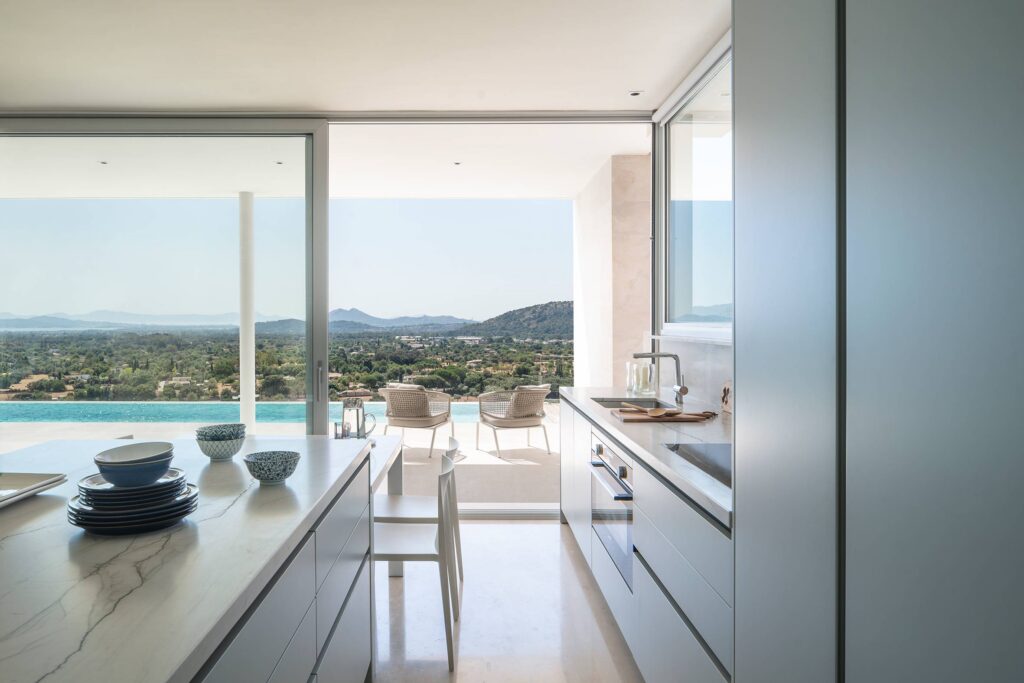 Cocina abierta a la terraza, isla con encimera veteada y vistas a la piscina y al valle