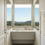 Baño con lavabo suspendido bajo una ventana con vistas a las montañas y radiador toallero blanco