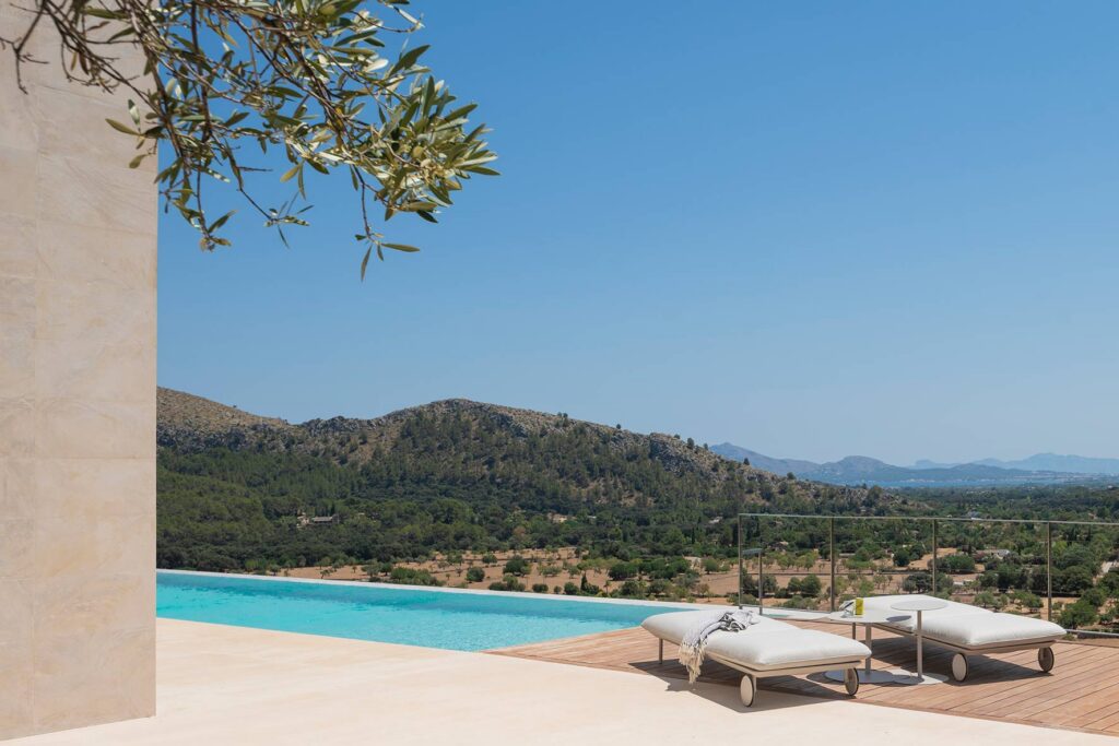 Tumbonas blancas junto a la piscina, con una rama de olivo y montañas verdes al fondo