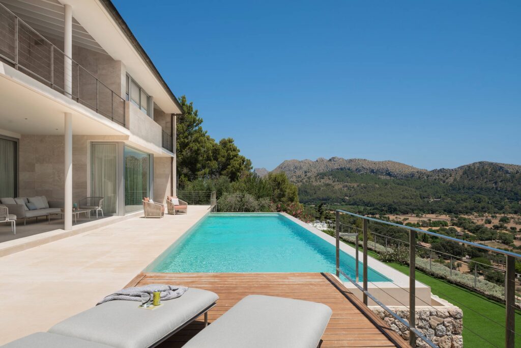 Fachada de la villa La Font con piscina infinita, terraza de piedra clara y montañas al fondo