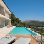 Fachada de la villa La Font con piscina infinita, terraza de piedra clara y montañas al fondo