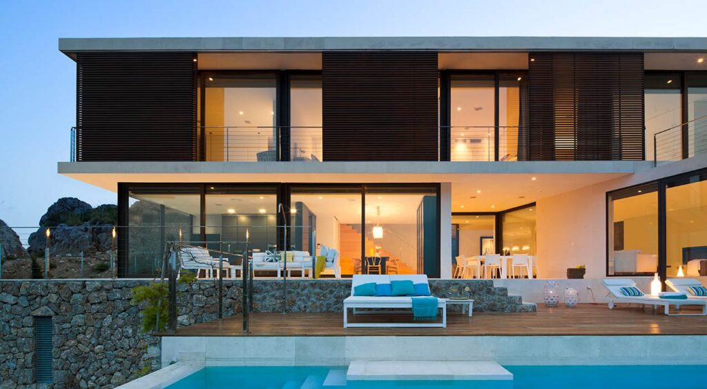 Fassade des Hauses LF115 in der Abenddämmerung mit Holzlamellen, Pool und beleuchteter Terrasse